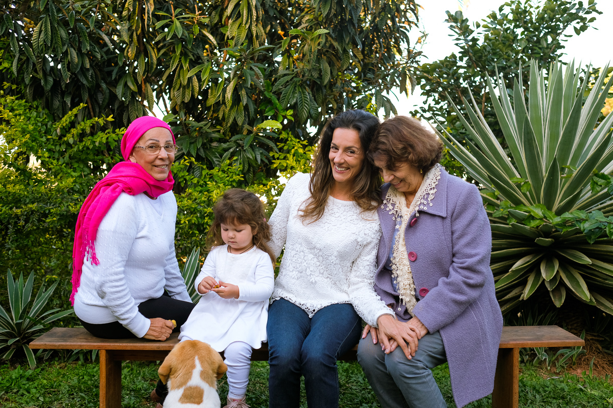 a criança sophie brinca com seu cachorro enquanto sua mãe e avós posam para retrato no ensaio de família fotografado pela fotógrafa de família Isis Vieira 