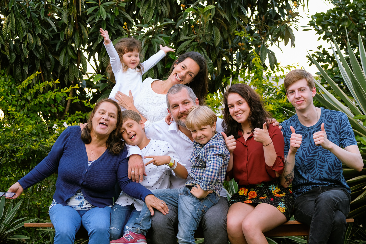 momento de muita alegria e descontração da família que se reuniu sentados num banco que fica no lindo jardim da casa para retrato de família em ensaio fotografado por Isis Vieira na lagoa da conceição em florianópolis 