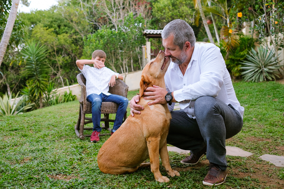 a cachorra da família lambe o nariz de seu dono em registro descontraído no jardim da casa da família em ensaio de família realizado na lagoa da conceição em florianópolis 