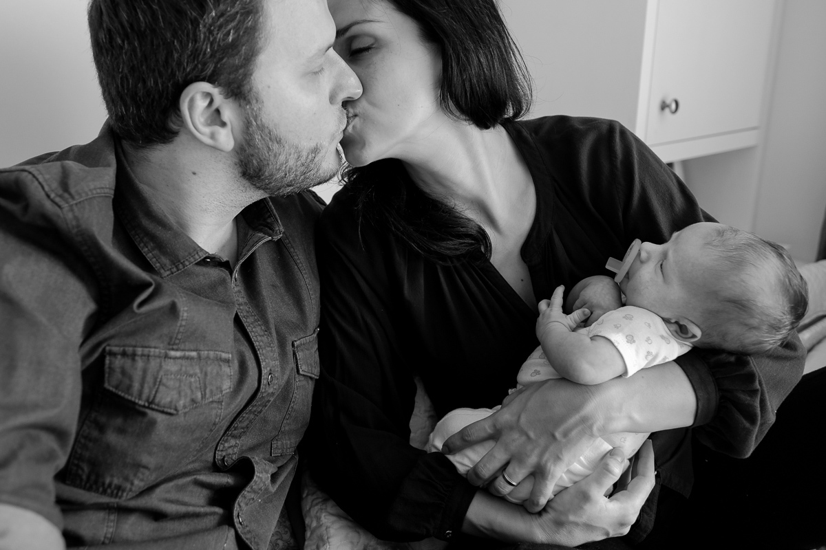 pai e mãe se beijam enquanto a mãe carrega o filho no colo em ensaio de família realizado em florianopolis no bairro do córrego grande