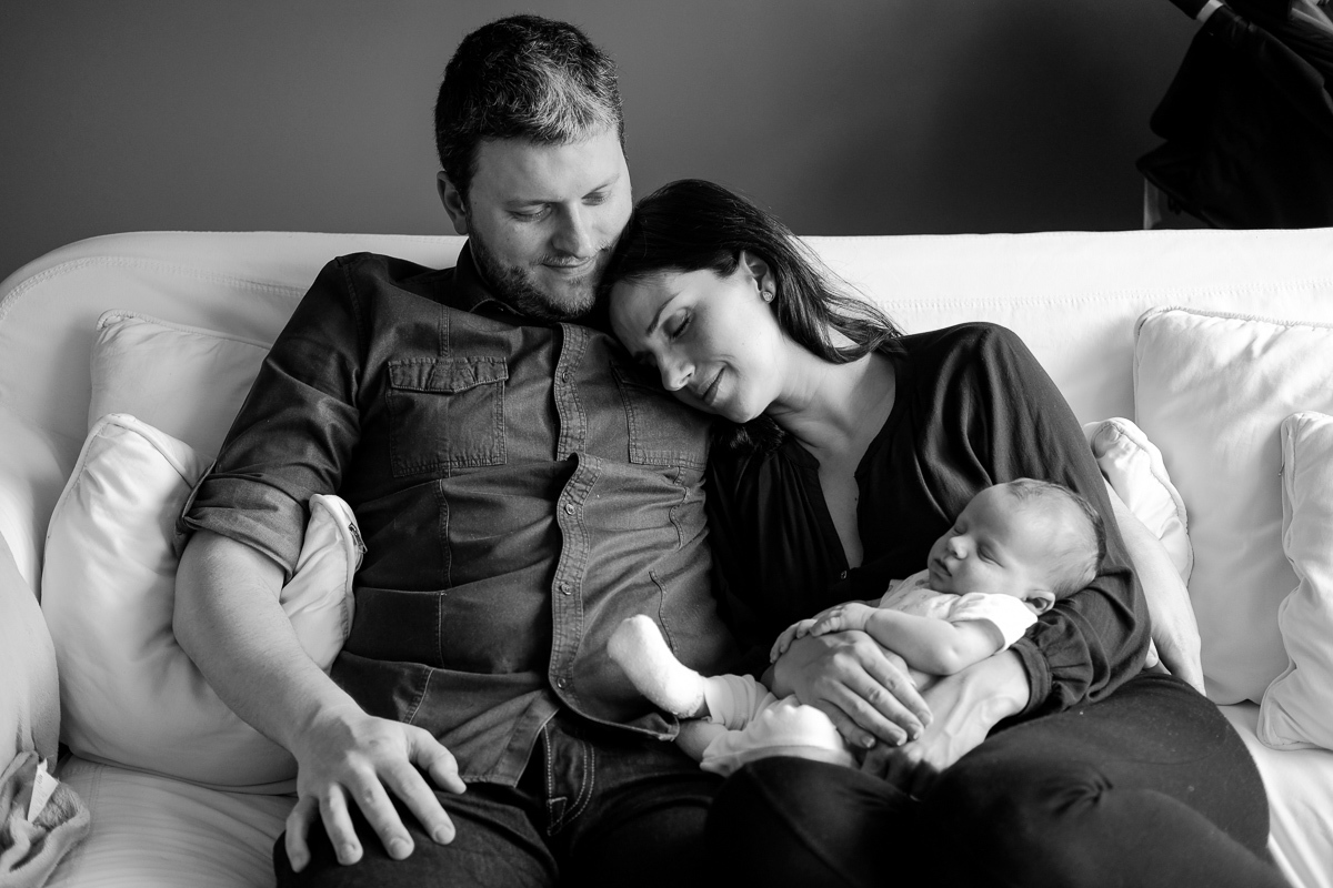 a mãe encosta no peito do marido em momento de amor e ternura com o recém nascido descansando em seu colo no ensaio fotografico de família realizado em florianopolis