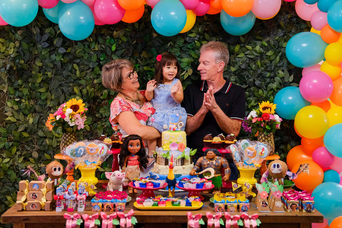 retrato da aniversariante Belinha com os avós na mesa decorada com tema Moana