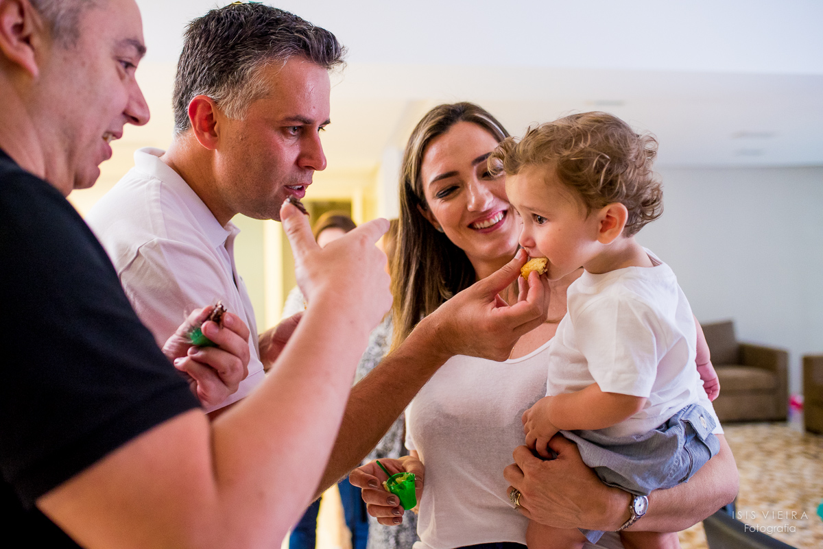 pai e mãe do pequeno aniversariante dando um pedaço de bolo para ele provar