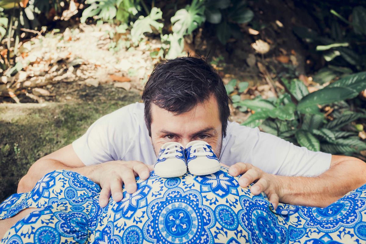 Papai se escondendo atrás da barriga da gestante e o sapatinho do bebê em ensaio de gestante