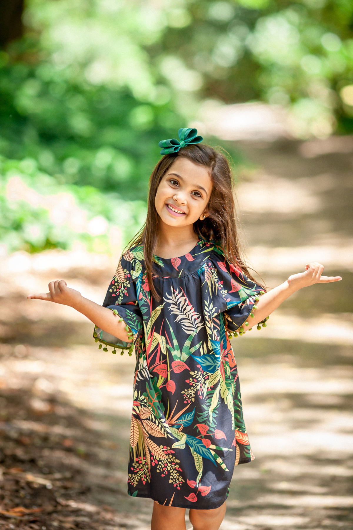 criança morena sorridente com vestido pompom azul com folhas de palmeiras na estampa durante editorial de moda clicado pelo fotógrafo queridinho do rio de janeiro paulo henrique lima