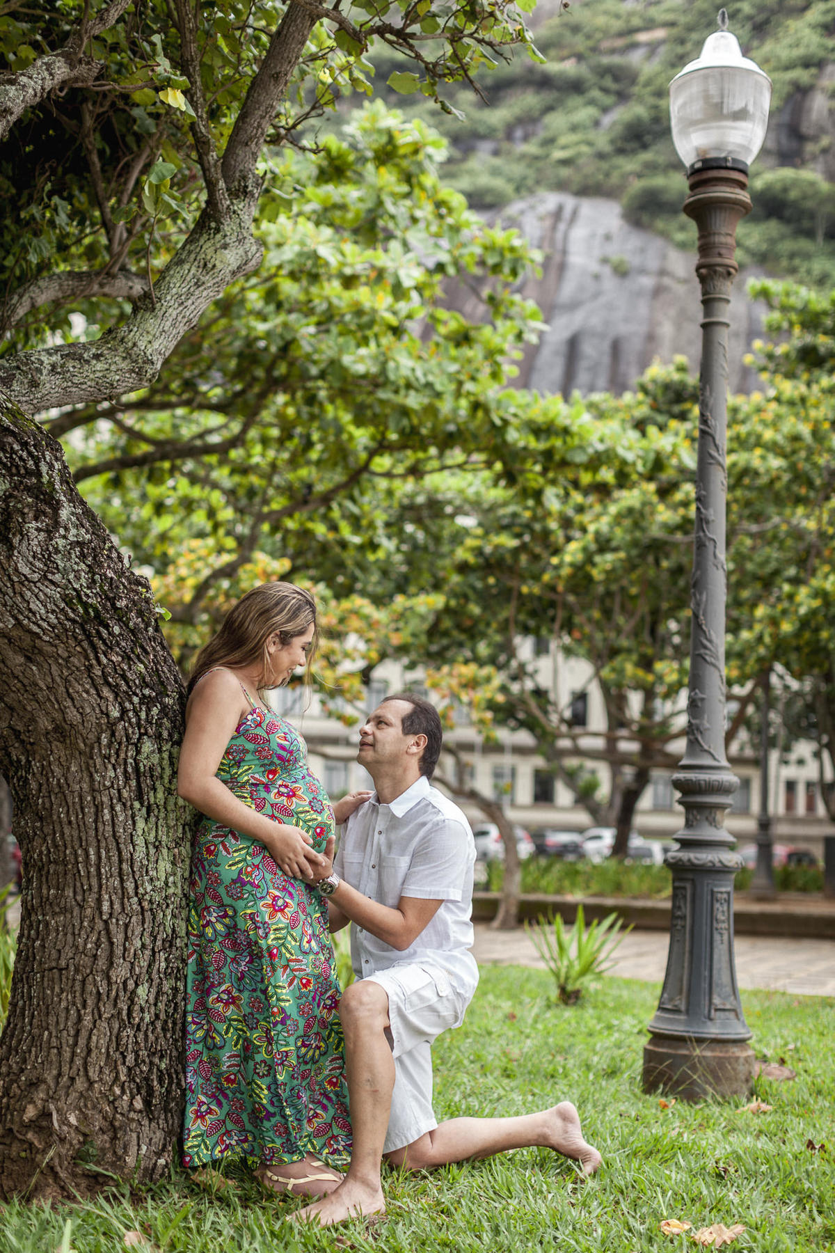 pai ajoelhado segurando barriga da mãe gestante em book fotográfico na praia vermelha rj