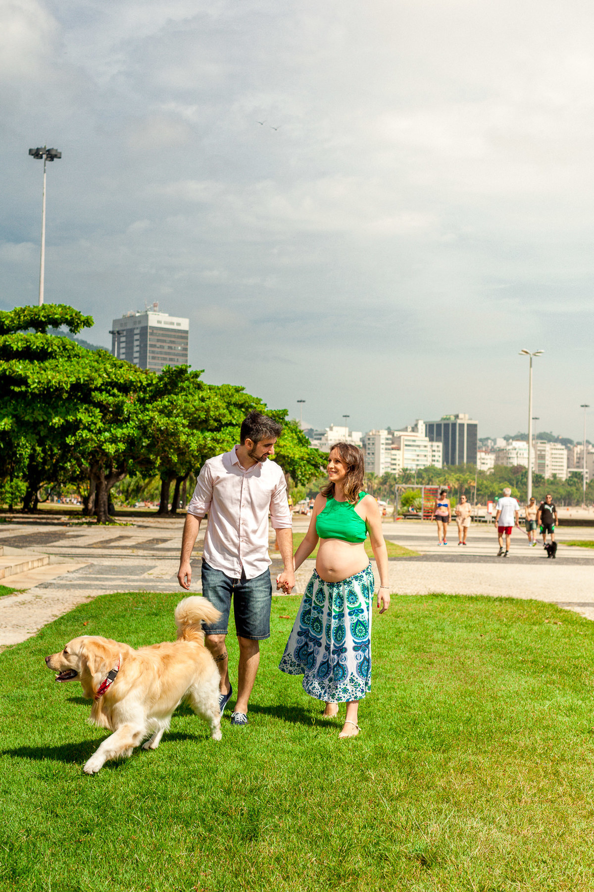 casal gestante caminhando pela grama de mãos dadas acompanhados do cachorro labrador