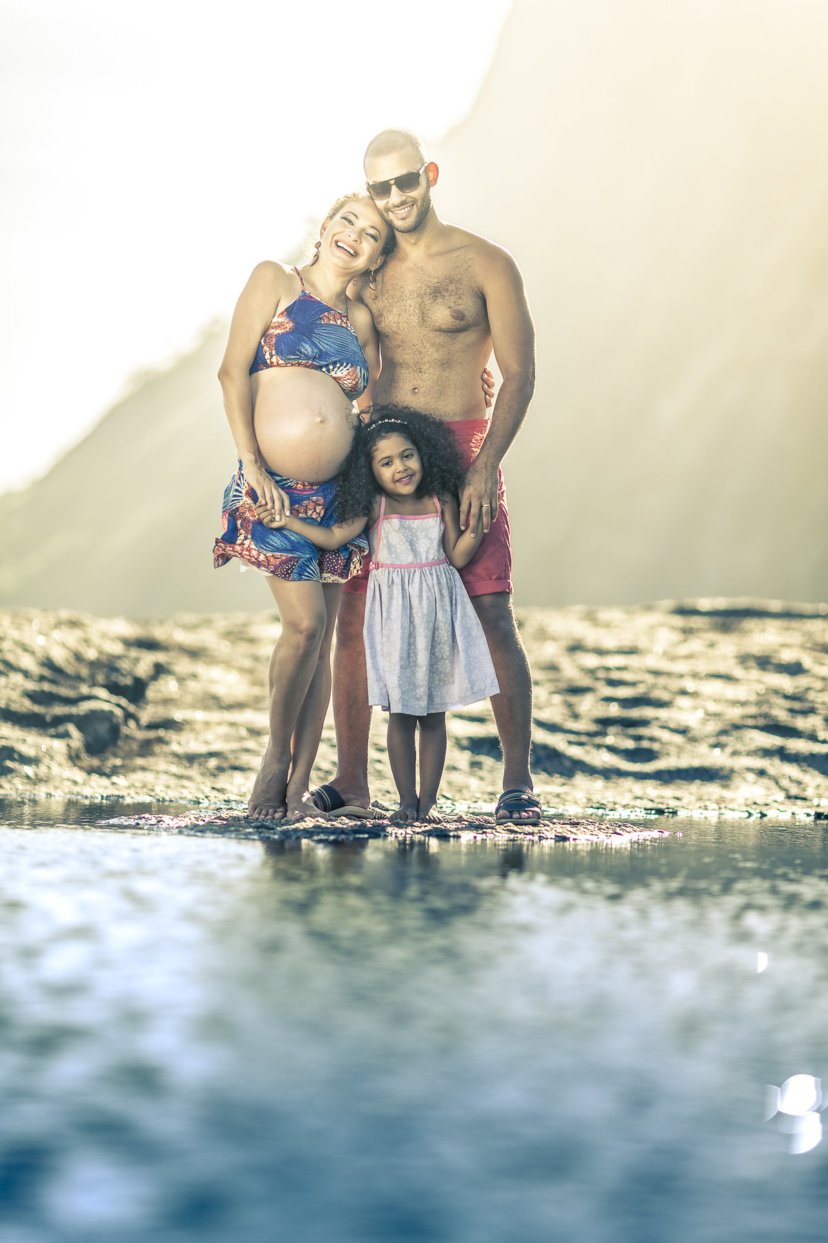 Gestante posando feliz com sua família em pedra de itaquatiara com sol em contra-luz