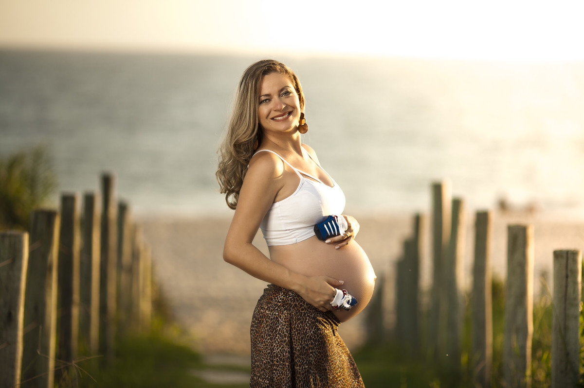 Gestante posando para foto com sapatinhos do filho sobre a barriga