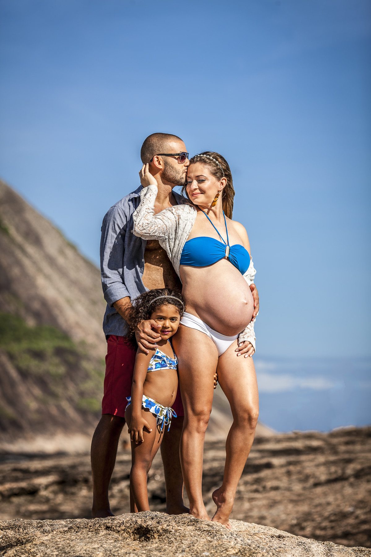 Casal Gestante trocando carinho com filha em pedra de itaquatiara em book de gestante