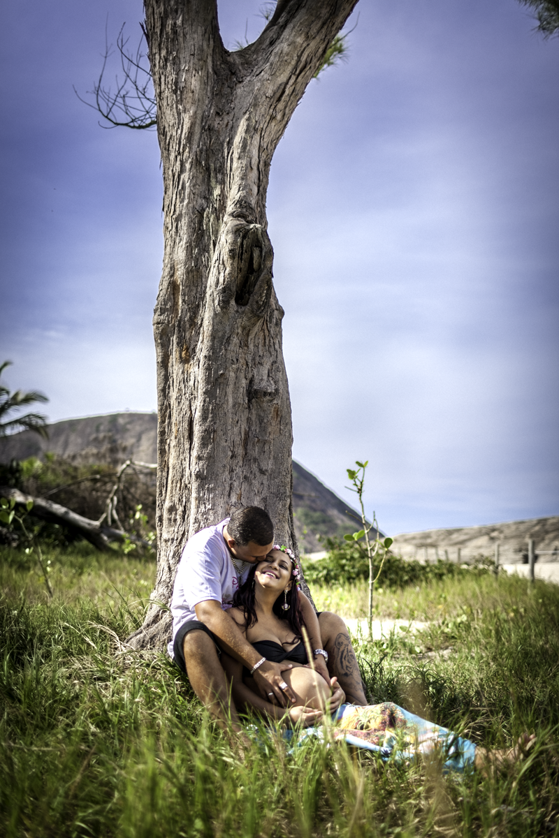 Gestante recebendo carinho do Papai embaixo de uma árvore em gramado verde na praia de itaquatiara