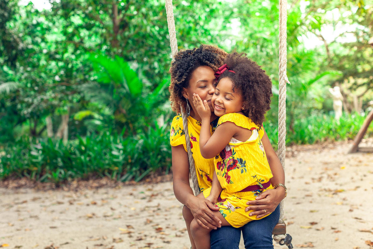 tal mãe tal filha em campanha publicitária de moda infantil com duas afrodescendentes mostrando a inclusão da marca para todas as etnias em poso super carinhosa mãe beijando filha no balanço de parque público no RJ pelo fotógrafo de publicidade paulohlima