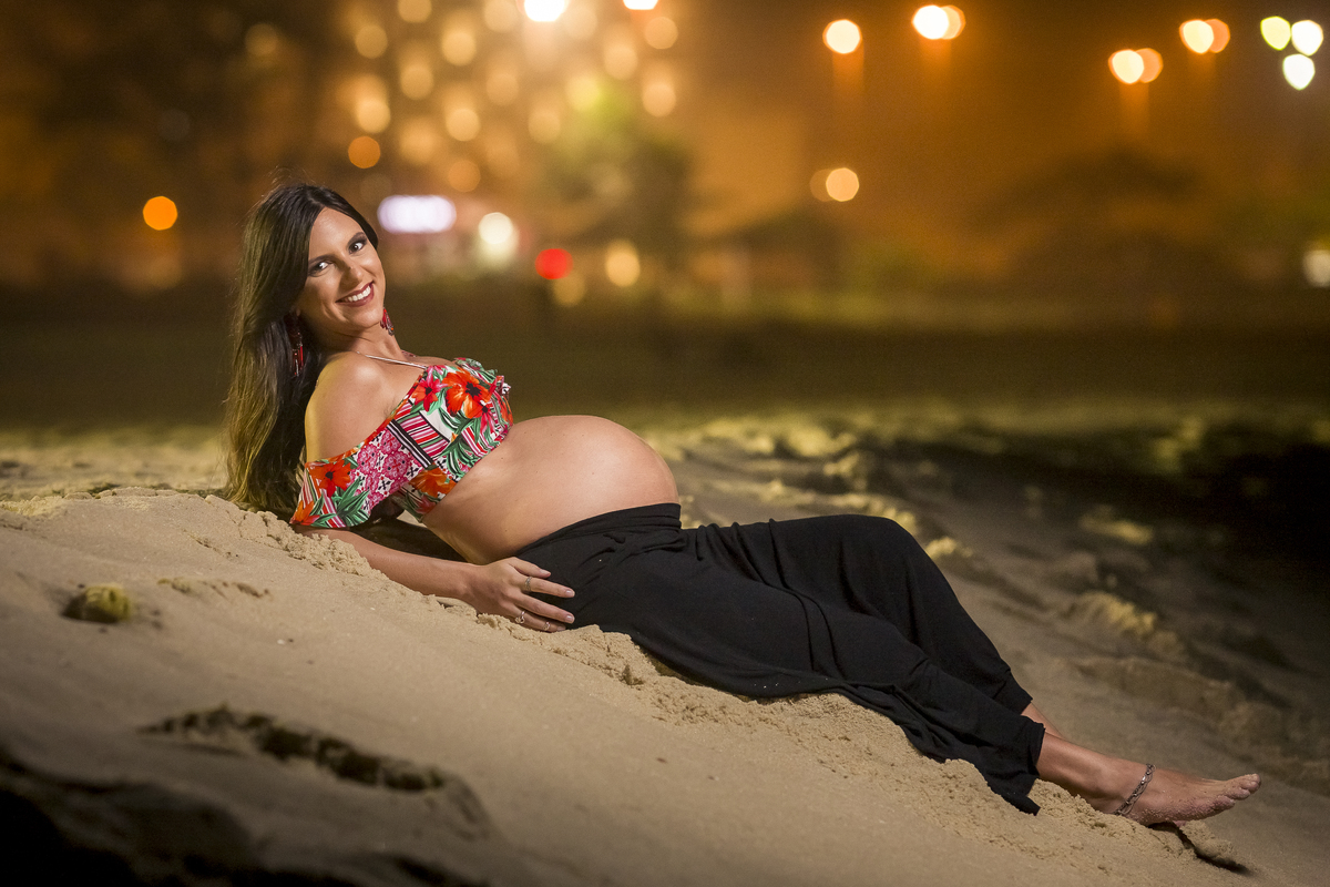 gestante posando para as lentes do fotógrafo de moda paulo henrique lima em ensaio de gestante noturno na praia do recreio deitada na arreia de barriga pra fora