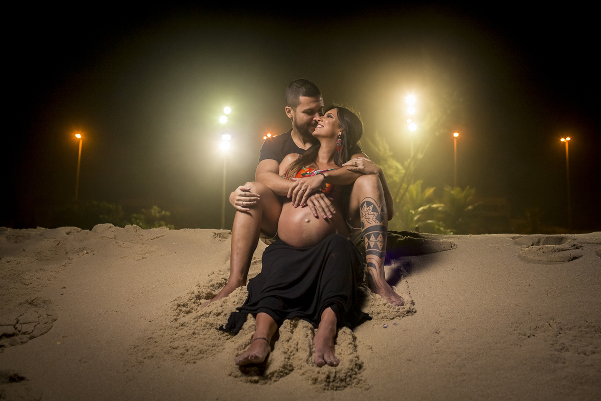 ensaio de gestante na praia do recreio rio de janeiro rj onde o casal esta sentado no areia de frente para o mar com a orla nas costas