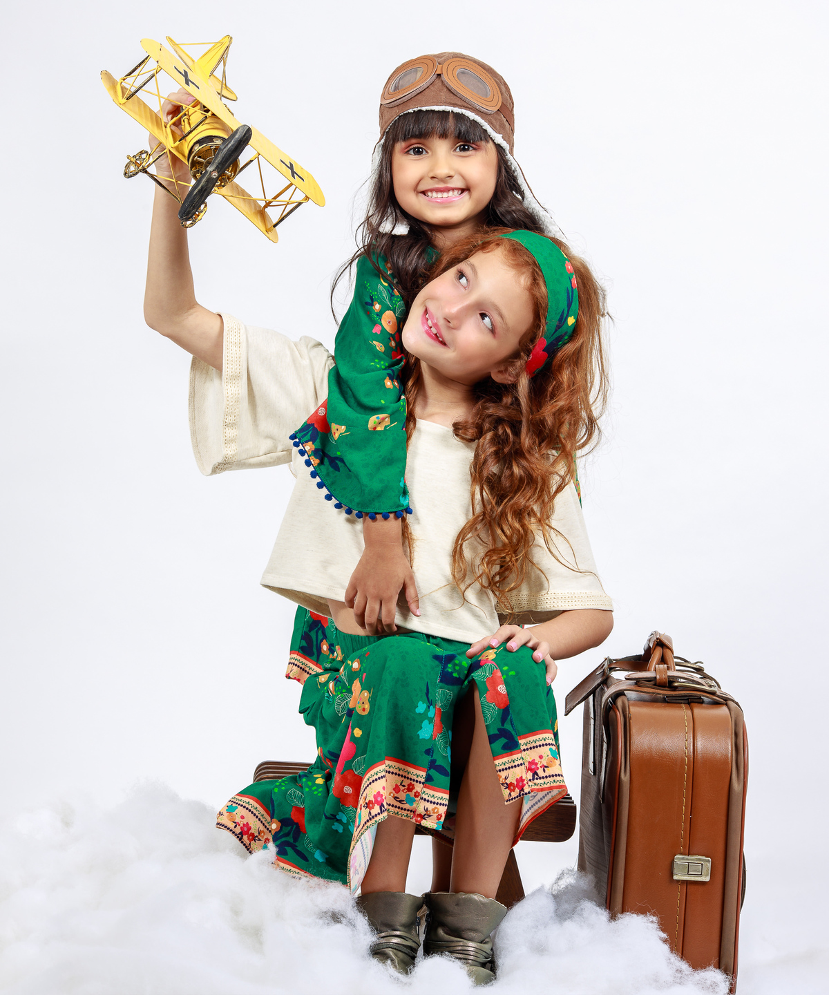 Campanha de Moda infantil com tema viajantes vestido verde avião amarelo mala de viajam crianças brincando